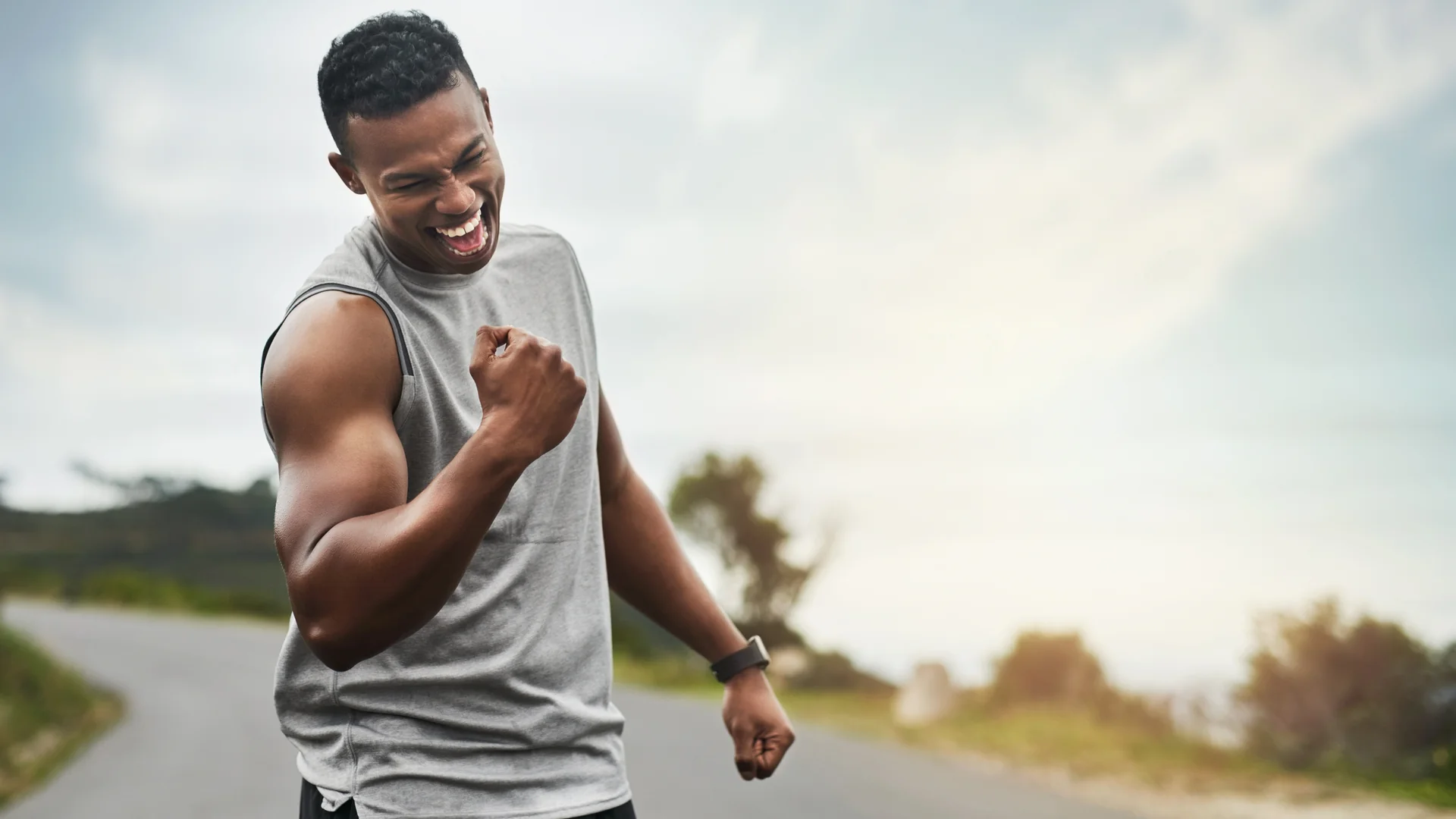 Man celebrating with a fist pump on an open road at sunrise