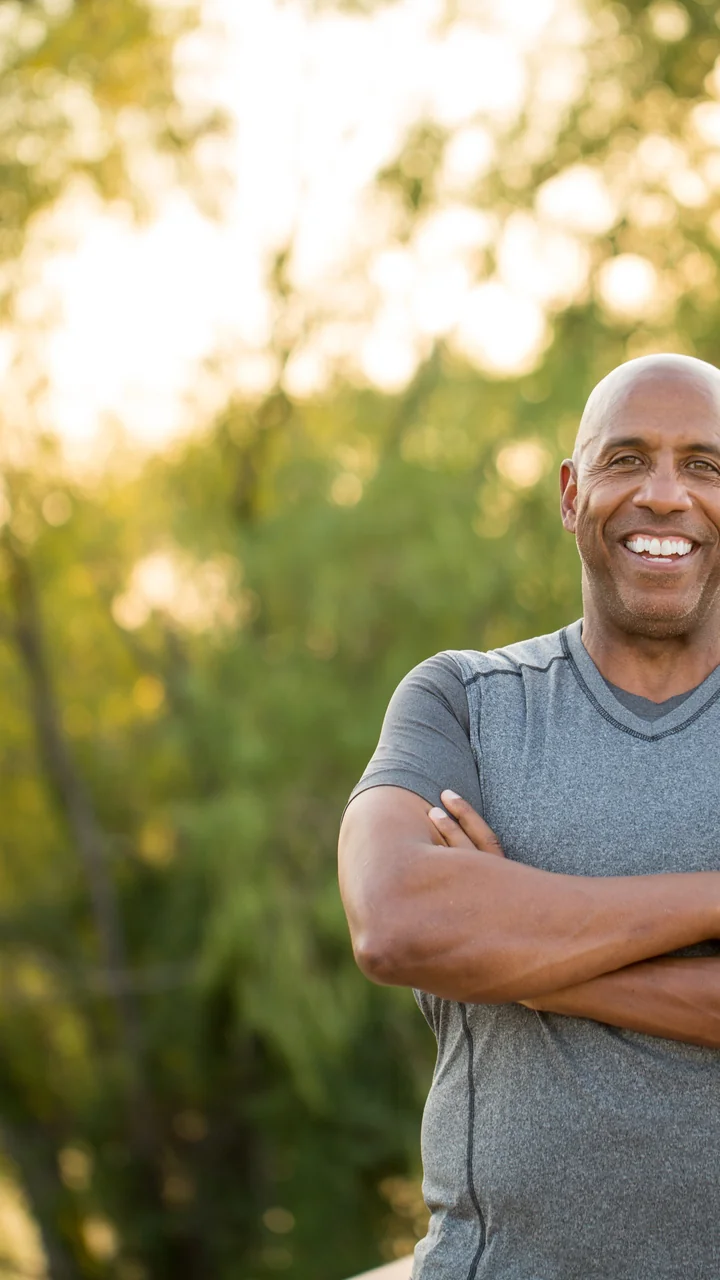 Bald mature Black man with arms crossed smiling outdoors in a park