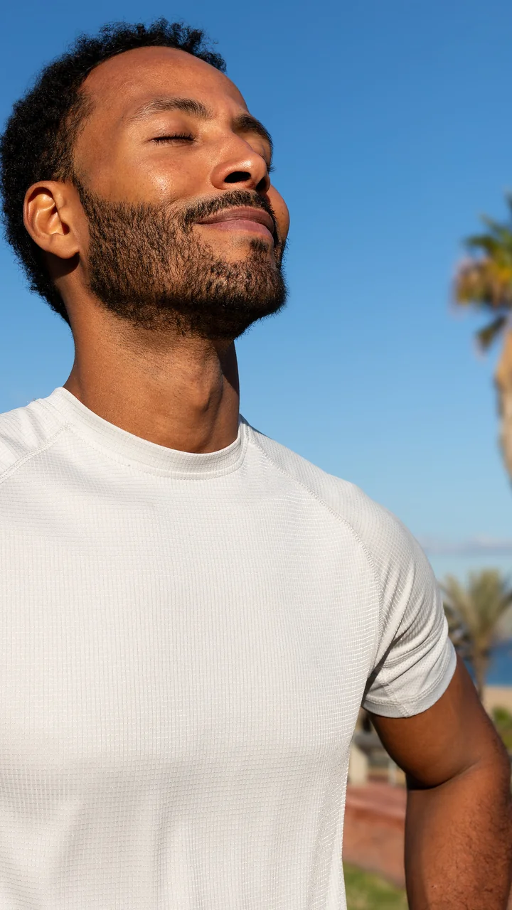 Young Black man eyes closed taking a deep breath at a palm-lined beach