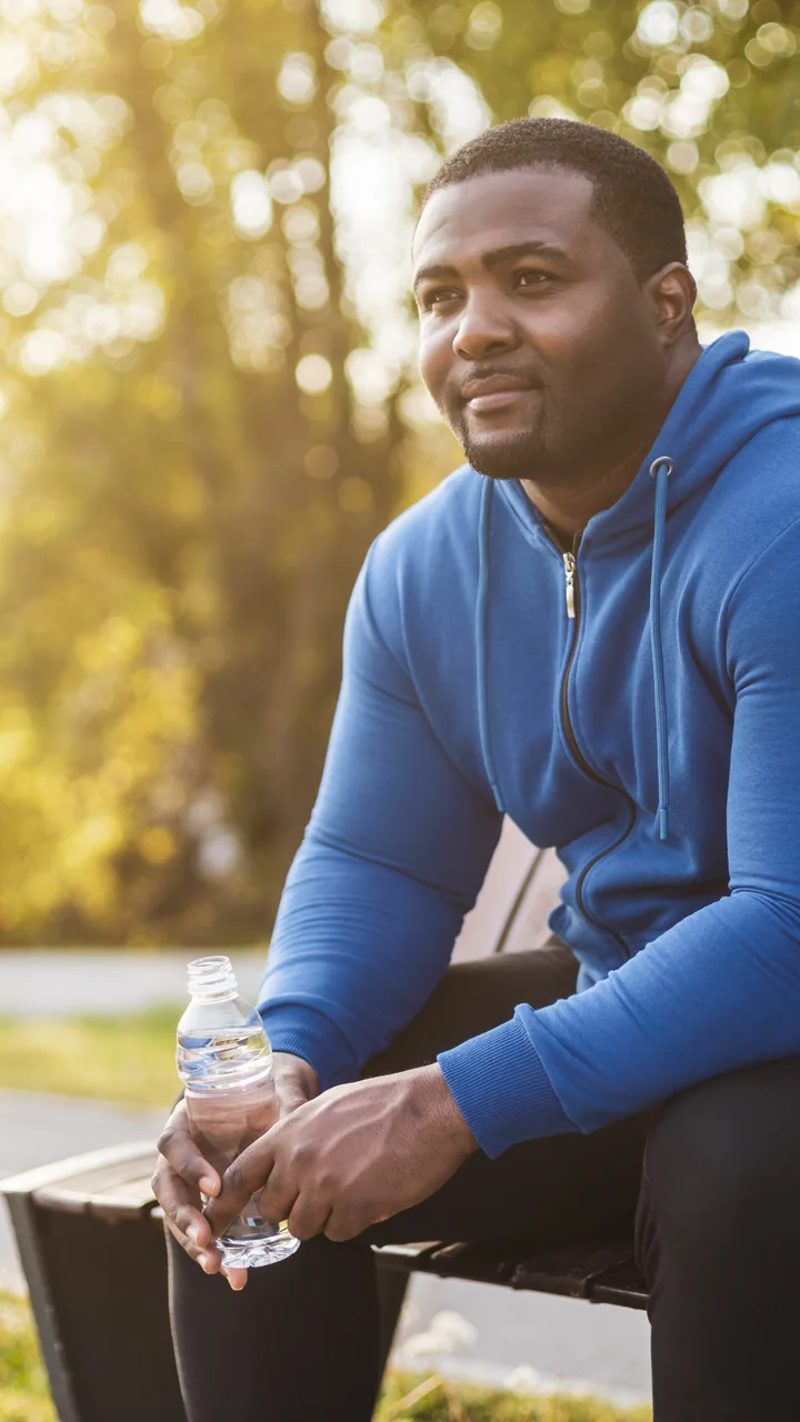 Man in a blue hoodie sitting on a park bench with a water bottle