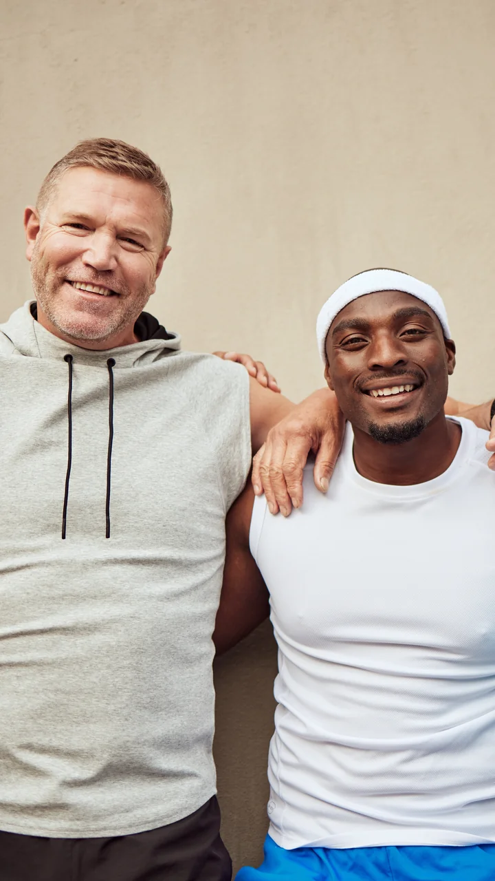 Four mature men of different ethnicities standing arm-in-arm, smiling