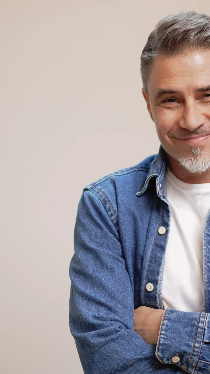 Mature man in a denim shirt with arms crossed against a taupe studio backdrop