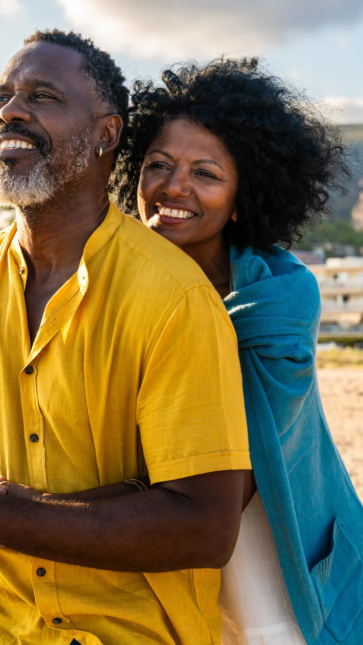 Older Black couple embracing on the beach at golden hour